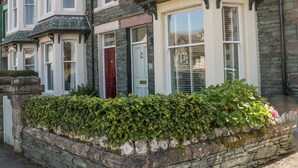 A traditional two-story house with a stone facade, a red door, and a well-maintained hedge in front.