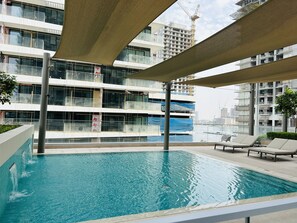 A modern hotel with a rooftop pool, multiple balconies, and a view of the city skyline. - StoneTree - Luxurious 1 BR with Private Beach Access (Dubai)