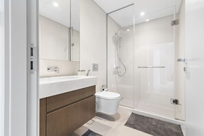 A modern bathroom with a glass shower enclosure, a white sink, and a toilet. - StoneTree - Luxurious 1 BR with Private Beach Access (Dubai)