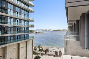 A modern multi-story building with a view of a calm body of water and a distant shoreline. - StoneTree - Luxurious 1 BR with Private Beach Access (Dubai)