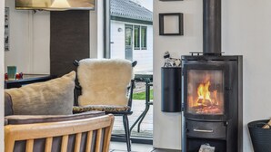 Ein gemütliches Wohnzimmer mit Kamin, einem an der Wand befestigten Fernseher und Blick auf ein Haus.