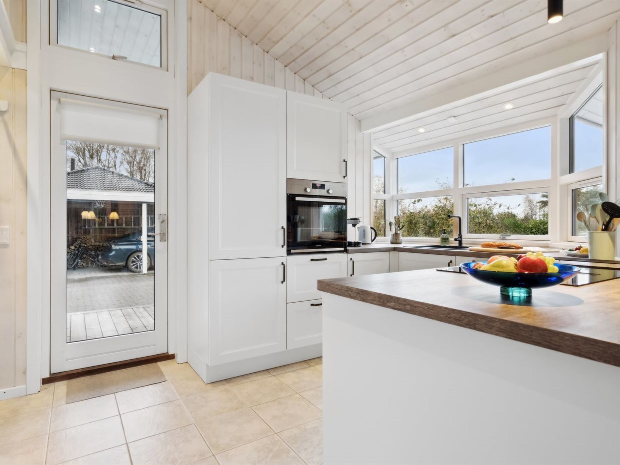 A modern kitchen with white cabinets, a built-in oven, and a large window.