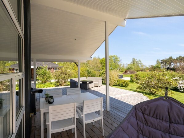 A covered patio with a table and chairs, a grill, and a view of a garden and neighboring houses.