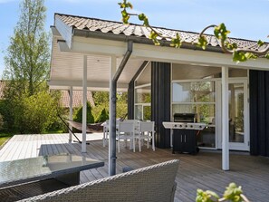 Une terrasse extérieure couverte, équipée d’un barbecue, de chaises blanches et d’une table à manger.