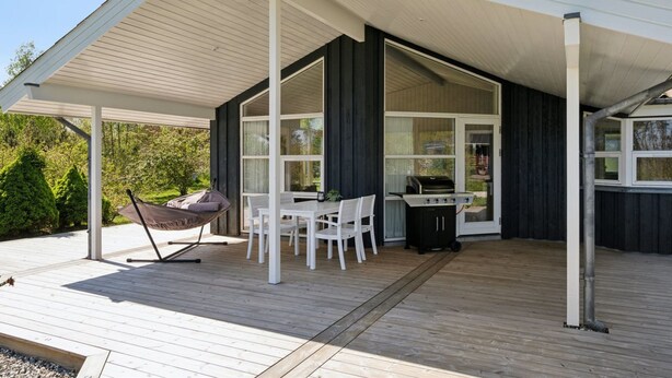 Een overdekte terras met een tafel, stoelen, een barbecue en een hangmat.