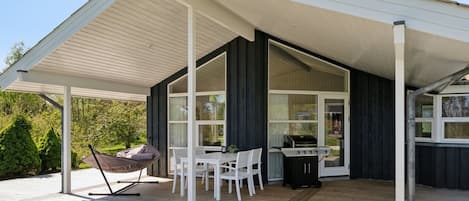 A covered outdoor patio with a table and chairs, a grill, and a hammock.