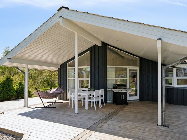 Une terrasse extérieure couverte, équipée d’une table et de chaises, d’un barbecue et d’un hamac.
