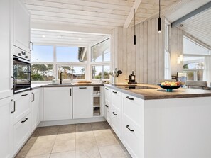Een moderne keuken met witte kastjes, een houten aanrechtblad en uitzicht op het groen.