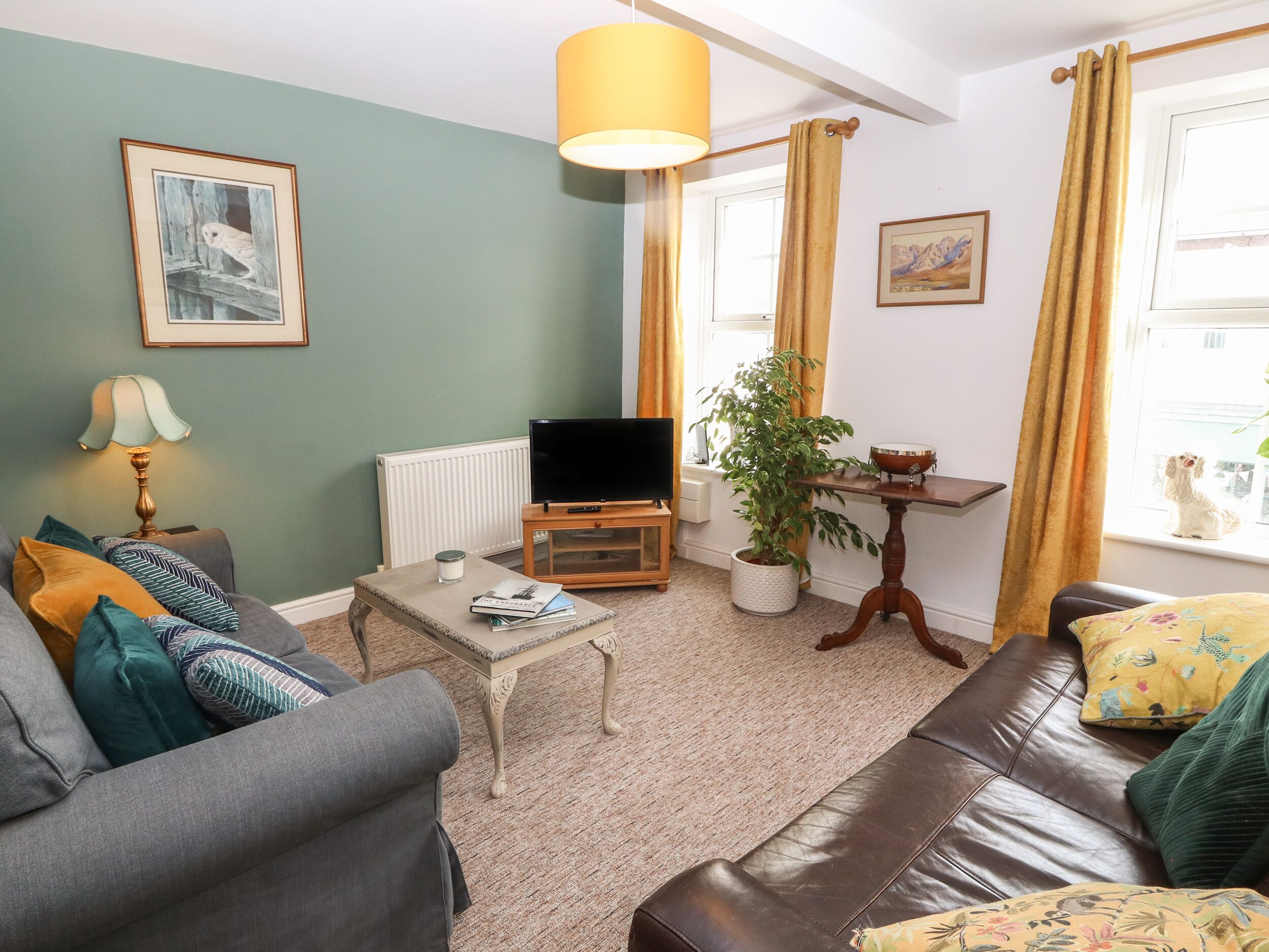 A living room with a grey sofa, a coffee table, a TV, a potted plant, and a window with curtains.