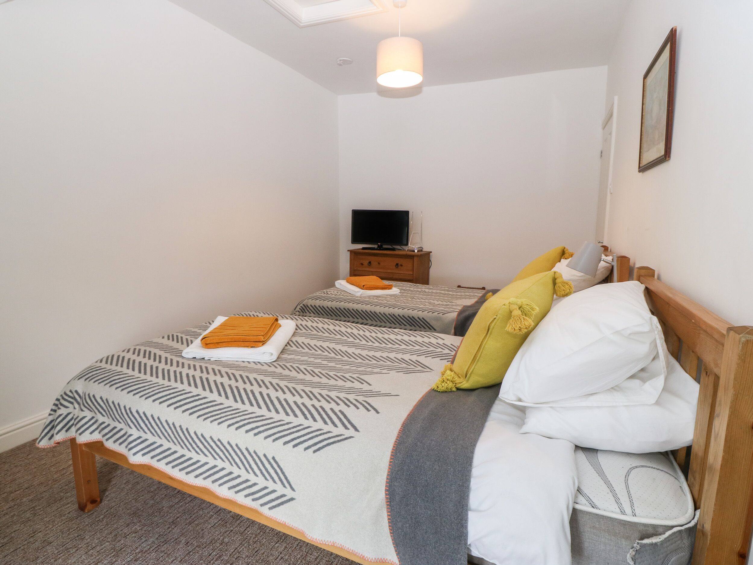 A bedroom with two beds, a television on a wooden nightstand, and a ceiling light.