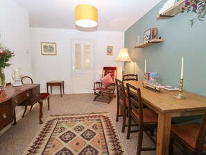A dining area with a wooden table, chairs, a rug, and a hanging lamp. - The Bell Apartment (Cemaes Bay)