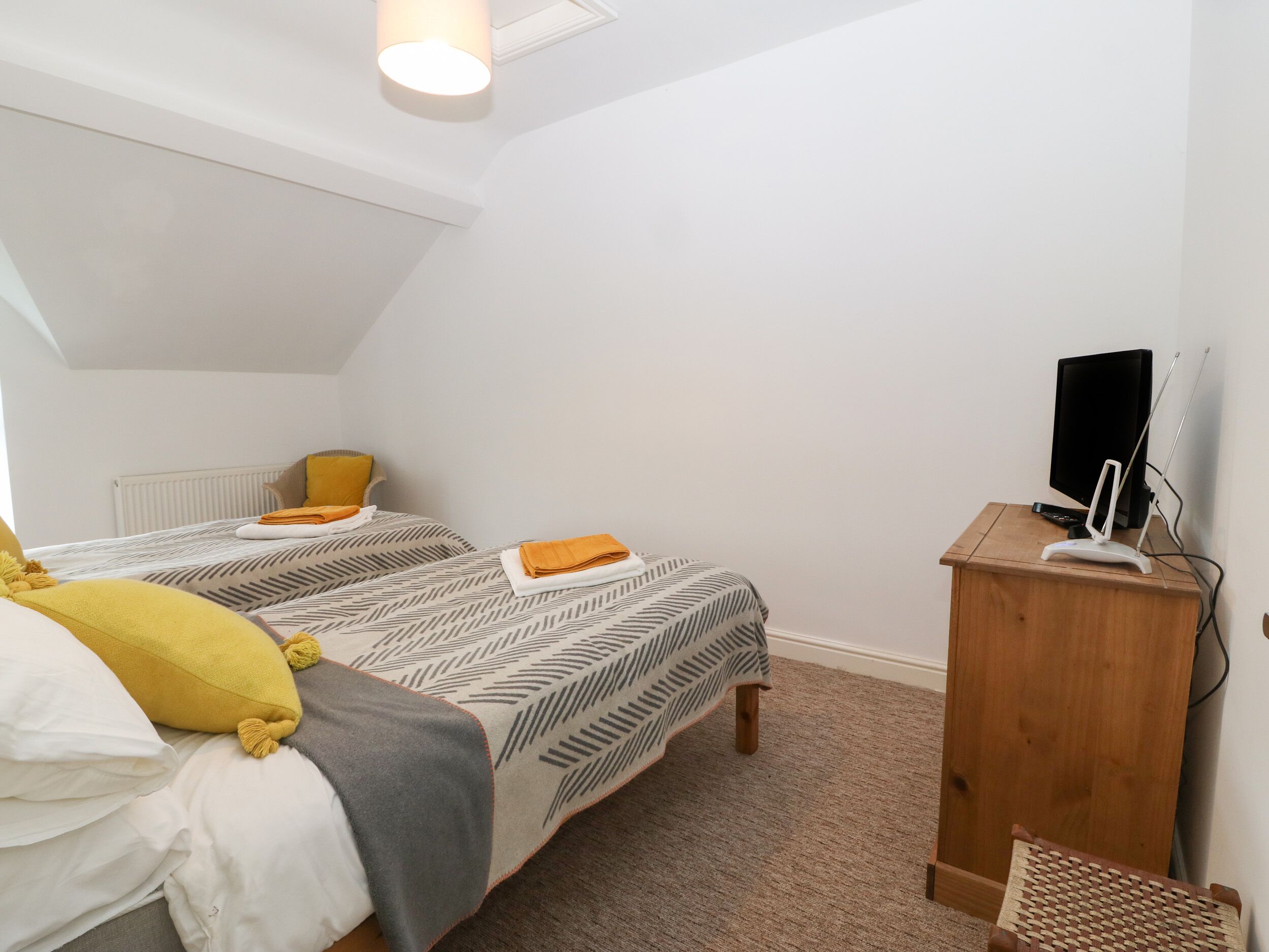 A bedroom with two beds, a wooden nightstand, a television, and a radiator.