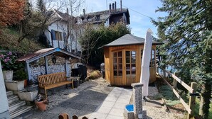 Eine Terrasse mit einer hölzernen Bank, einer kleinen Holzhütte und einer Steinmauer.