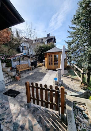 Relax in a serene outdoor space surrounded by trees, featuring a sauna or hot tub and a paved stone area.