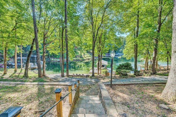 A pathway leading to a lake surrounded by trees, with a view of buildings in the background.