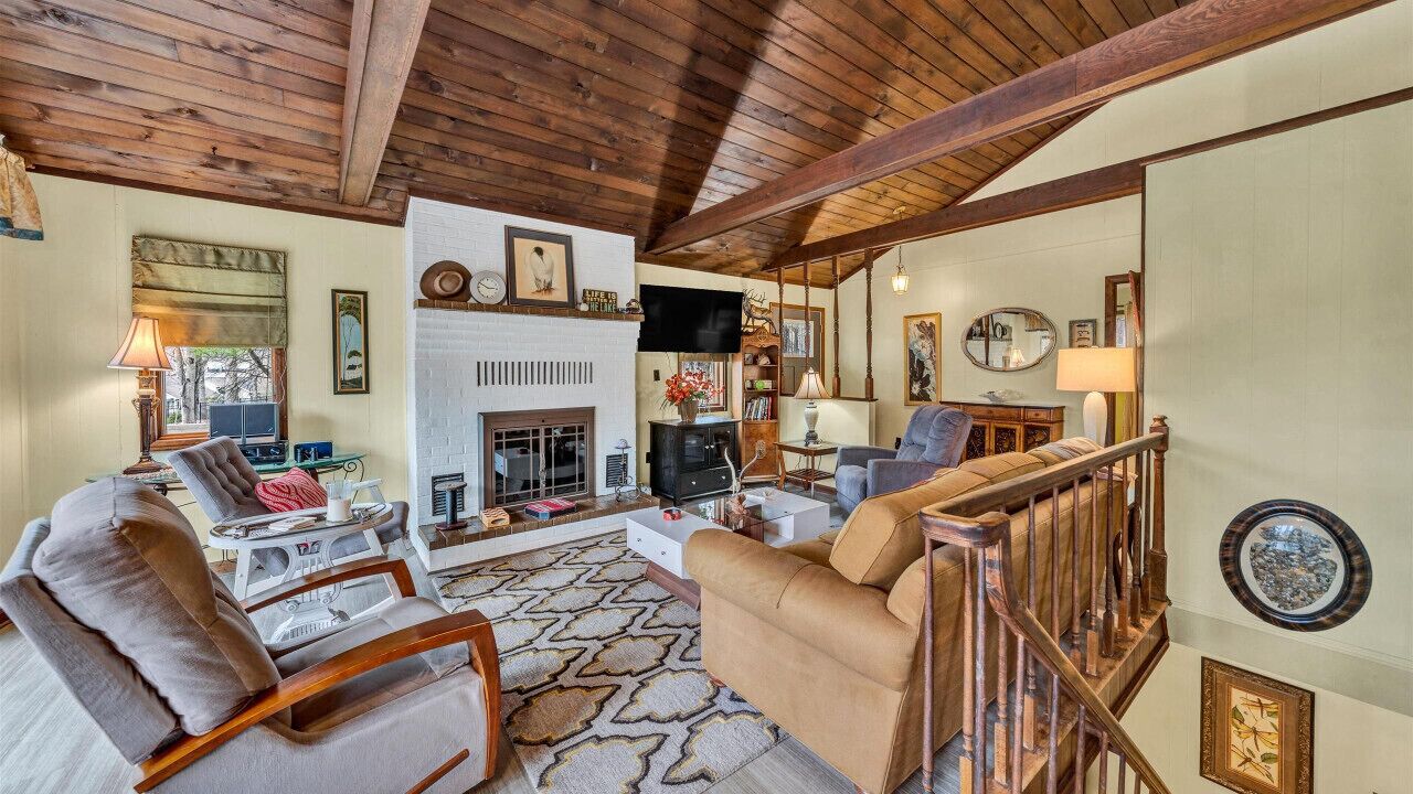 A cozy living room with a fireplace, wooden beams, and a staircase.