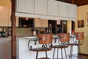 A kitchen with white cabinets, a stainless steel microwave, and a bar area with four stools.
