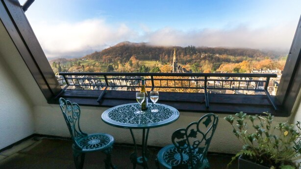 Un balcon avec deux chaises et une table, offrant une vue panoramique sur un village et des montagnes.