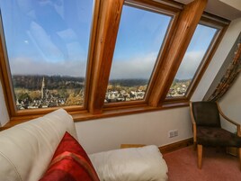 A room with a view of a town through large windows, a white sofa, and a dark armchair.