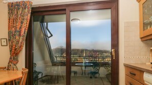 Une pièce dotée d’une porte-fenêtre coulissante donnant sur un balcon avec une table et des chaises, une table à manger en bois, et un coin cuisine avec des placards et un plan de travail.