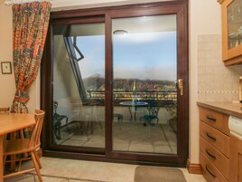 A room with a sliding glass door leading to a balcony with a table and chairs, a wooden dining table, and a kitchen area with cabinets and a countertop.