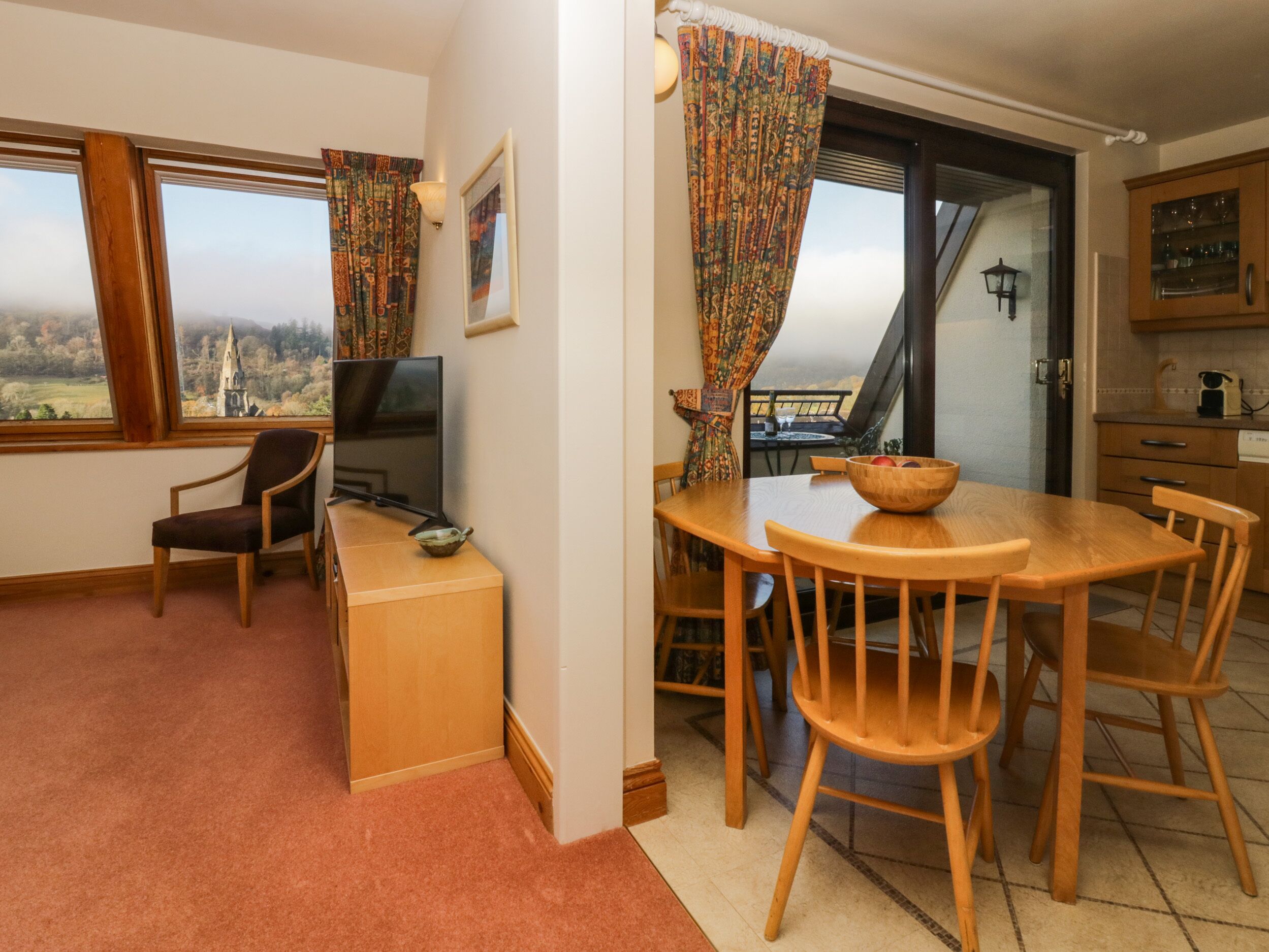 A cozy room with a wooden dining table, chairs, a TV, and a view of a church through the window.