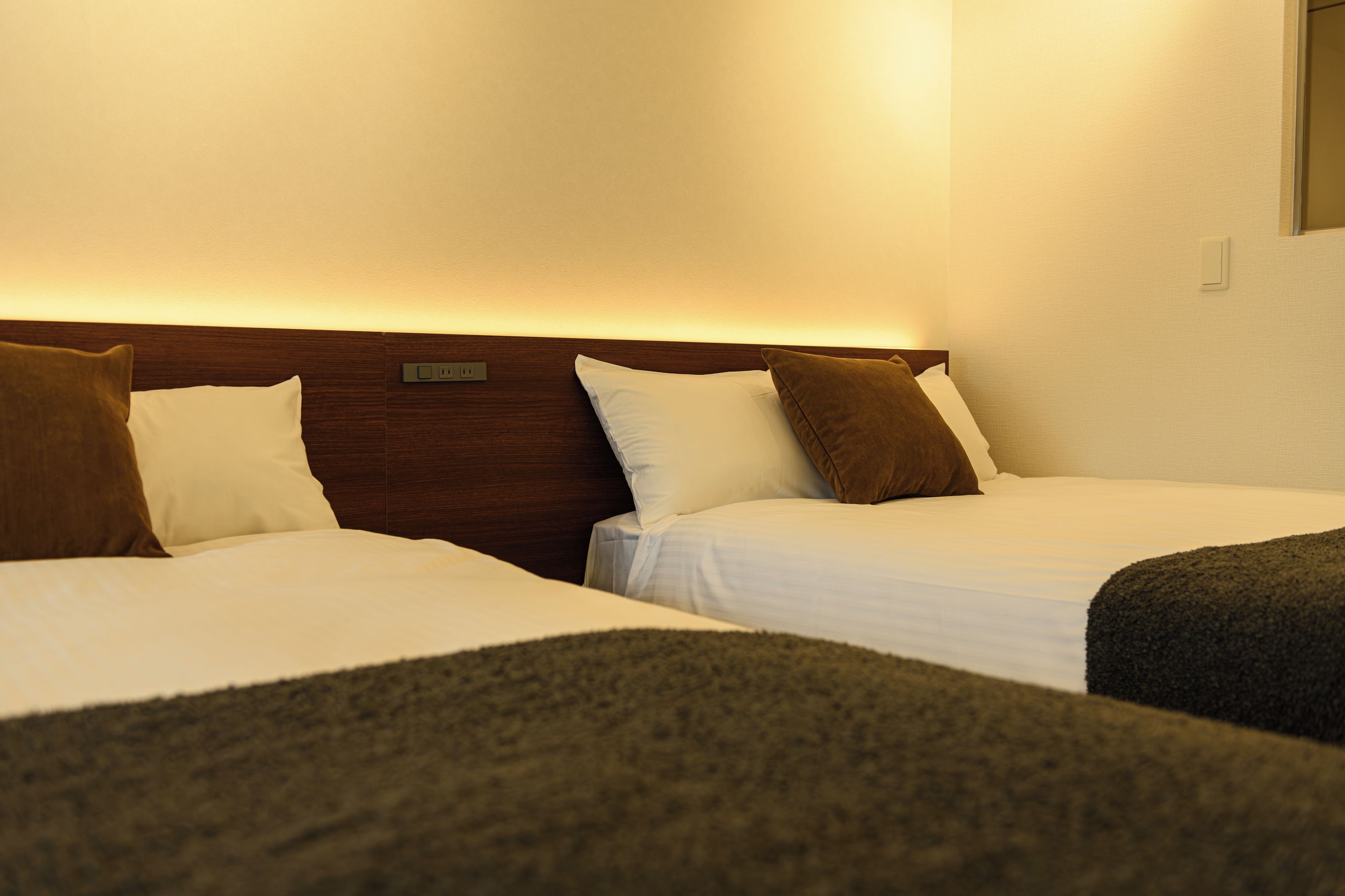 A hotel room with two beds, a wooden headboard, and a bedside table with a lamp.