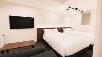 Ein Hotelzimmer mit zwei Betten, einem Flachbildfernseher, einer hölzernen Bank und einem kleinen Sofa.