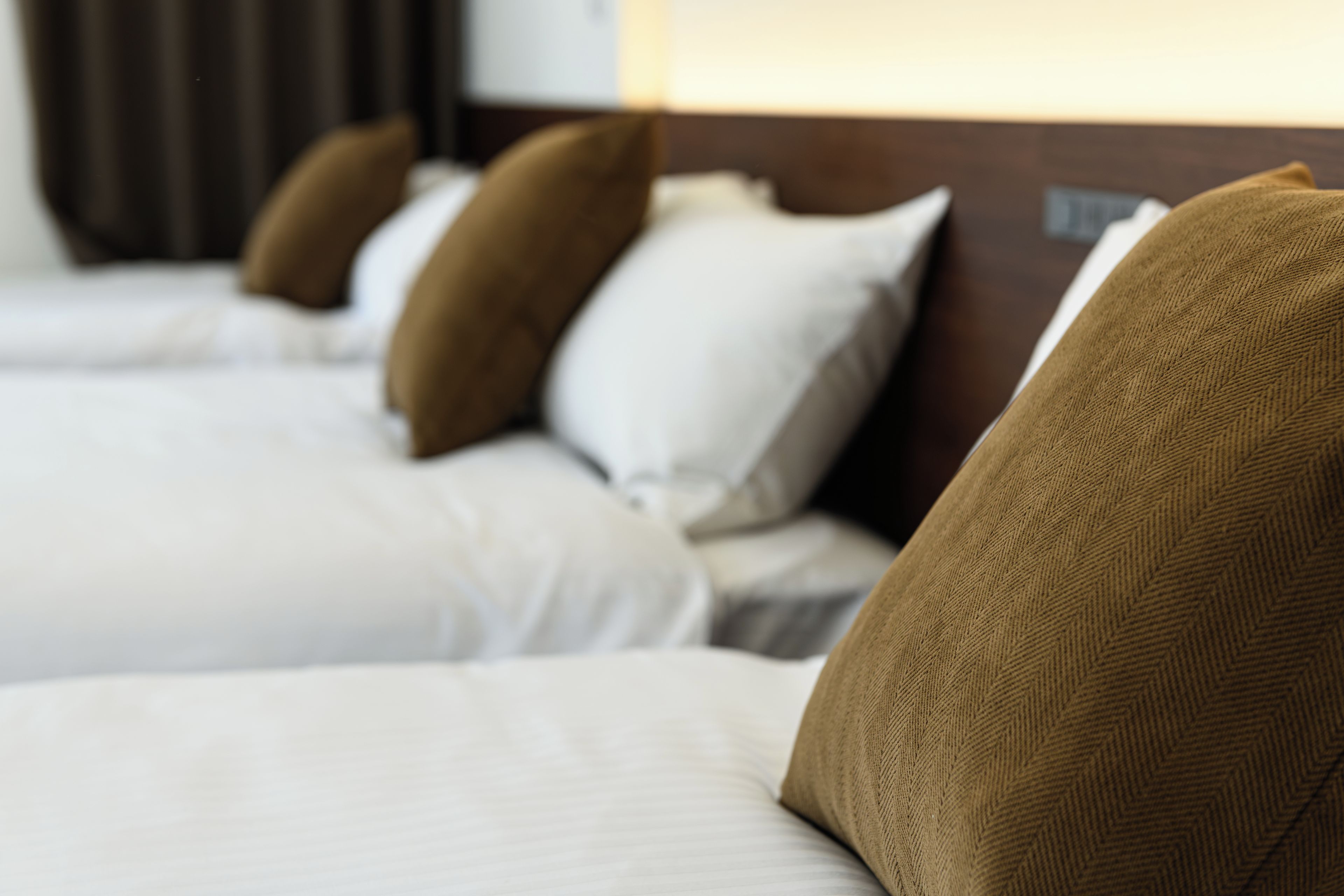 A hotel room with a row of beds, each with a brown pillow and white bedding.