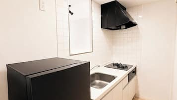 Una cocina compacta con armarios blancos, un refrigerador negro, una estufa y una campana extractora negra.