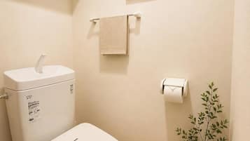 Un baño moderno con inodoro, estante con plantas, un cuadro enmarcado, toallero y un cesto de basura.