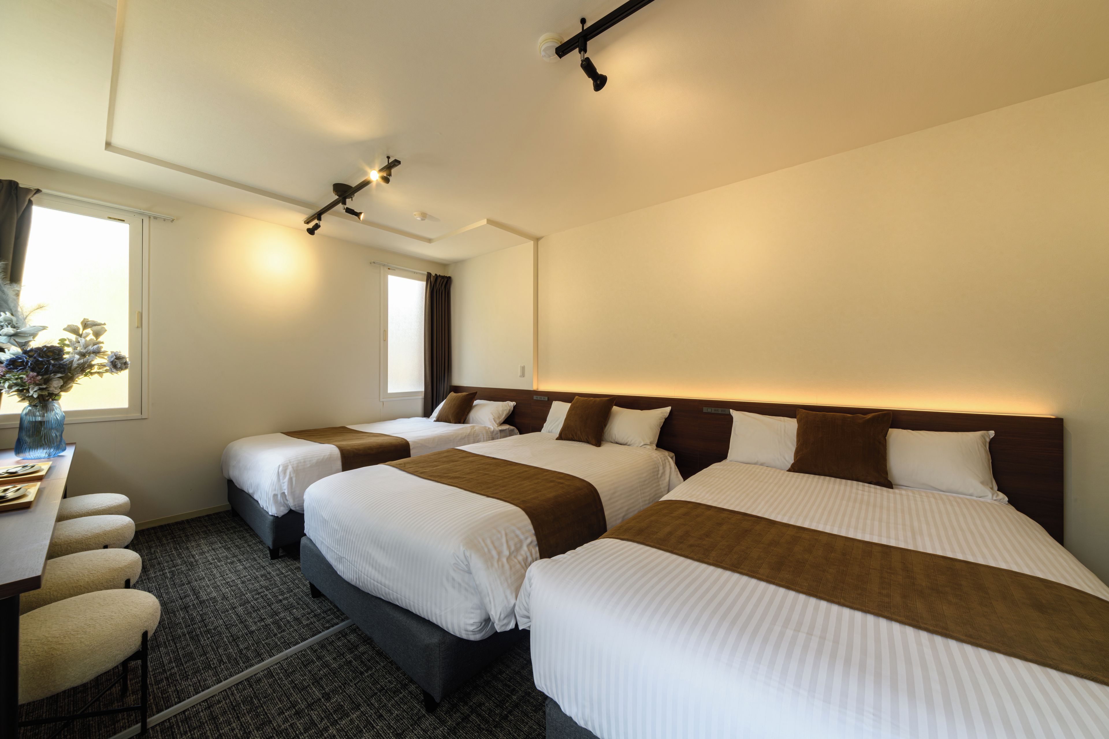 A hotel room with three beds, a desk, and a window.