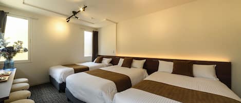 A hotel room with three beds, a desk, and a window.