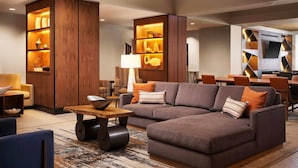 Un salon moderne avec un canapé d’angle, des étagères en bois et un coin repas comprenant une table et des chaises.