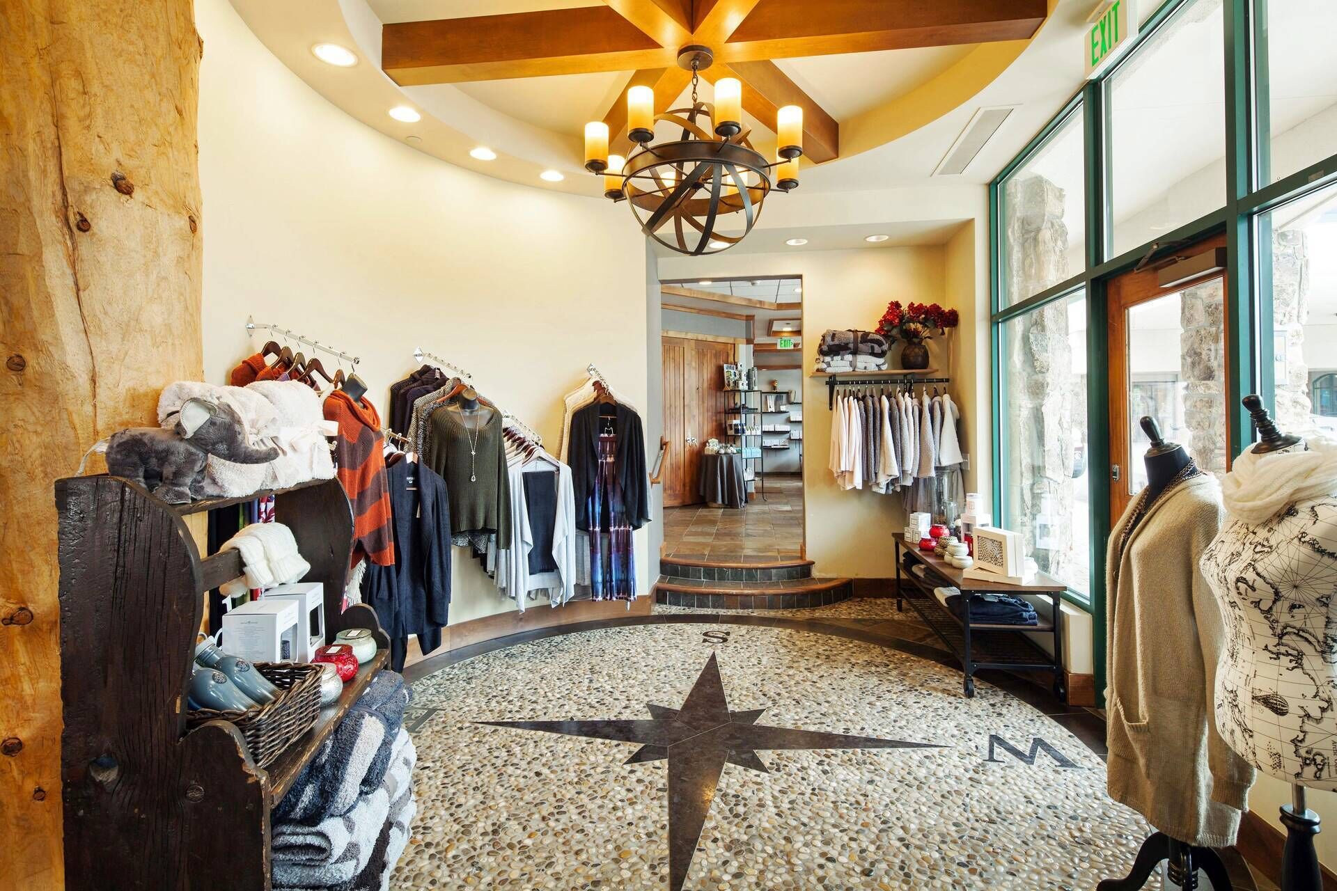 A boutique hotel lobby with a central mosaic floor, clothing racks, and a chandelier.