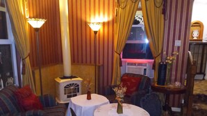 A cozy room with striped wallpaper, a fireplace, a sofa, two tables with floral tablecloths, and a decorative vase. - All Season's Groveland Inn  (Groveland)