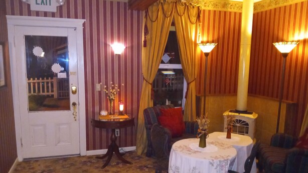 A room with striped wallpaper, a round table with a floral tablecloth, a small side table with a lamp, and a chair. - All Season's Groveland Inn  (Groveland)