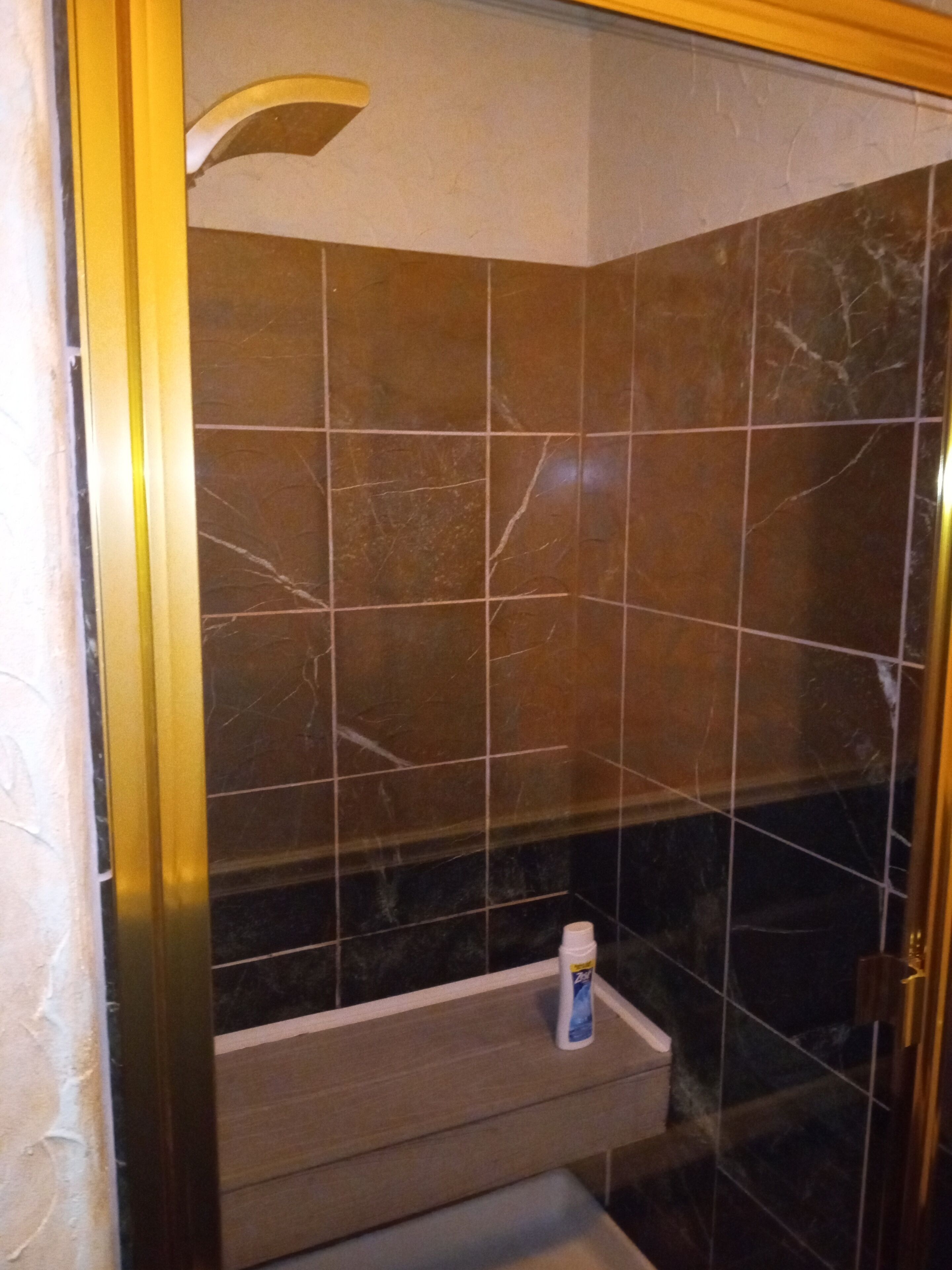 Une salle de bain avec des carreaux de marbre foncé, un banc en bois et un flacon de savon pour les mains.