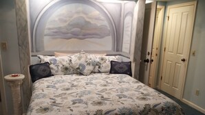 A bedroom with a large bed, floral bedding, a decorative headboard, a bedside table, and a door. - All Season's Groveland Inn  (Groveland)