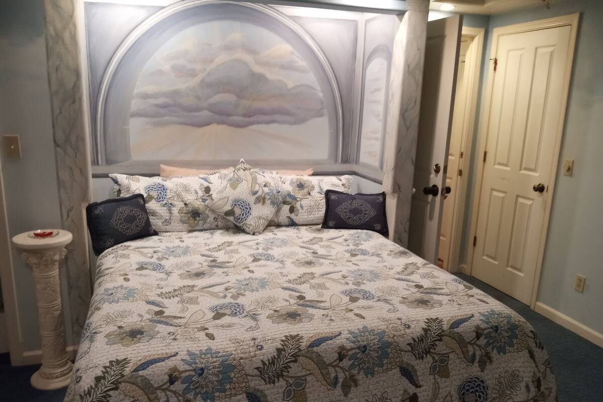 A bedroom with a large bed, floral bedding, a decorative headboard, a bedside table, and a door.