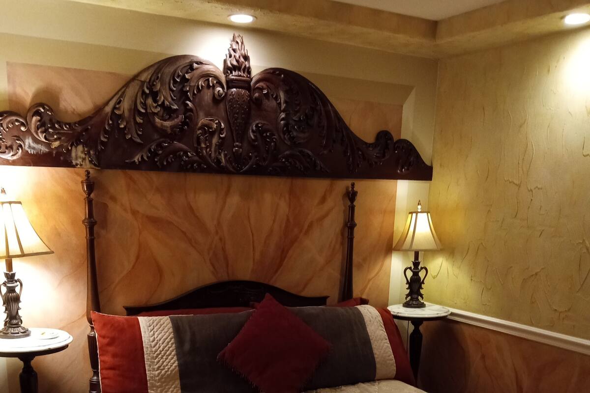 A hotel room with a large bed, ornate headboard, two bedside tables with lamps, and a floral-patterned bedspread.