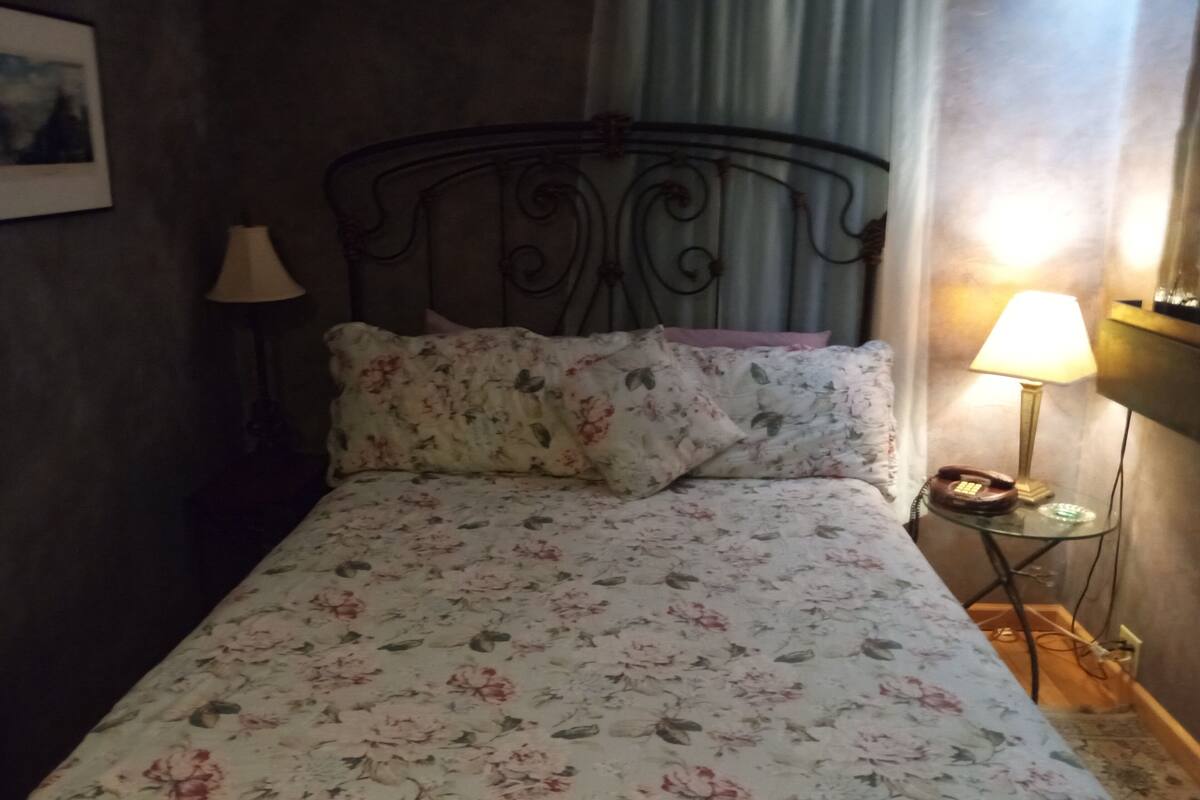 A bed with floral bedding, a bedside lamp, and a telephone on a small table beside the bed.
