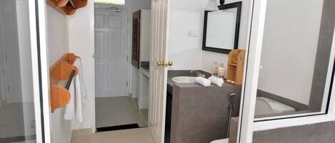Baño con inodoro, lavabo y espejo. Hay un perchero y una puerta que da a otra habitación.