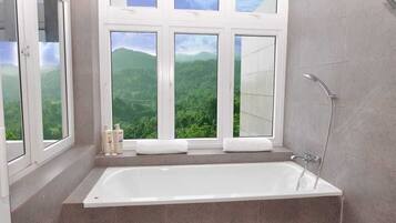 A bathroom with a bathtub, a shower, and a window with a mountain view.
