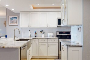 A modern kitchen with white cabinets, a marble countertop, a built-in oven, and a microwave. - Beachfront Unit at Lands End. Beautiful Resort. Heated Pools, Hot Tubs & Tennis. (Treasure Island)