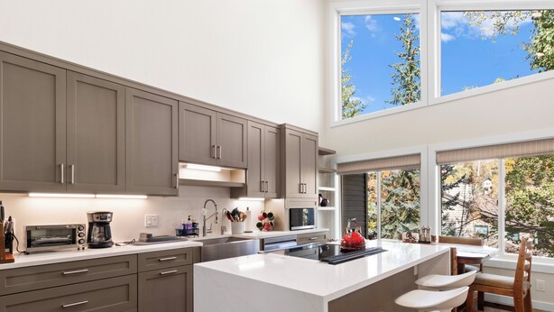 Una cocina moderna con una isla grande, electrodomésticos integrados y vistas a árboles a través de amplios ventanales.