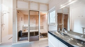 Ett modernt badrum med en träpanelbeklädd bastu, en stor spegel och en tvättställskombination med bänkskiva.