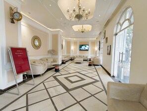 A spacious lobby with a geometric patterned floor, a chandelier, and a television screen. - Jewels Resorts (Jaipur)