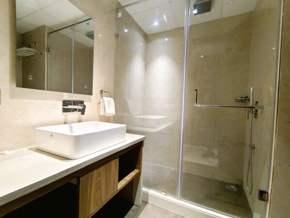 Un baño moderno con un espejo grande, un lavabo blanco y una ducha con mampara de vidrio.