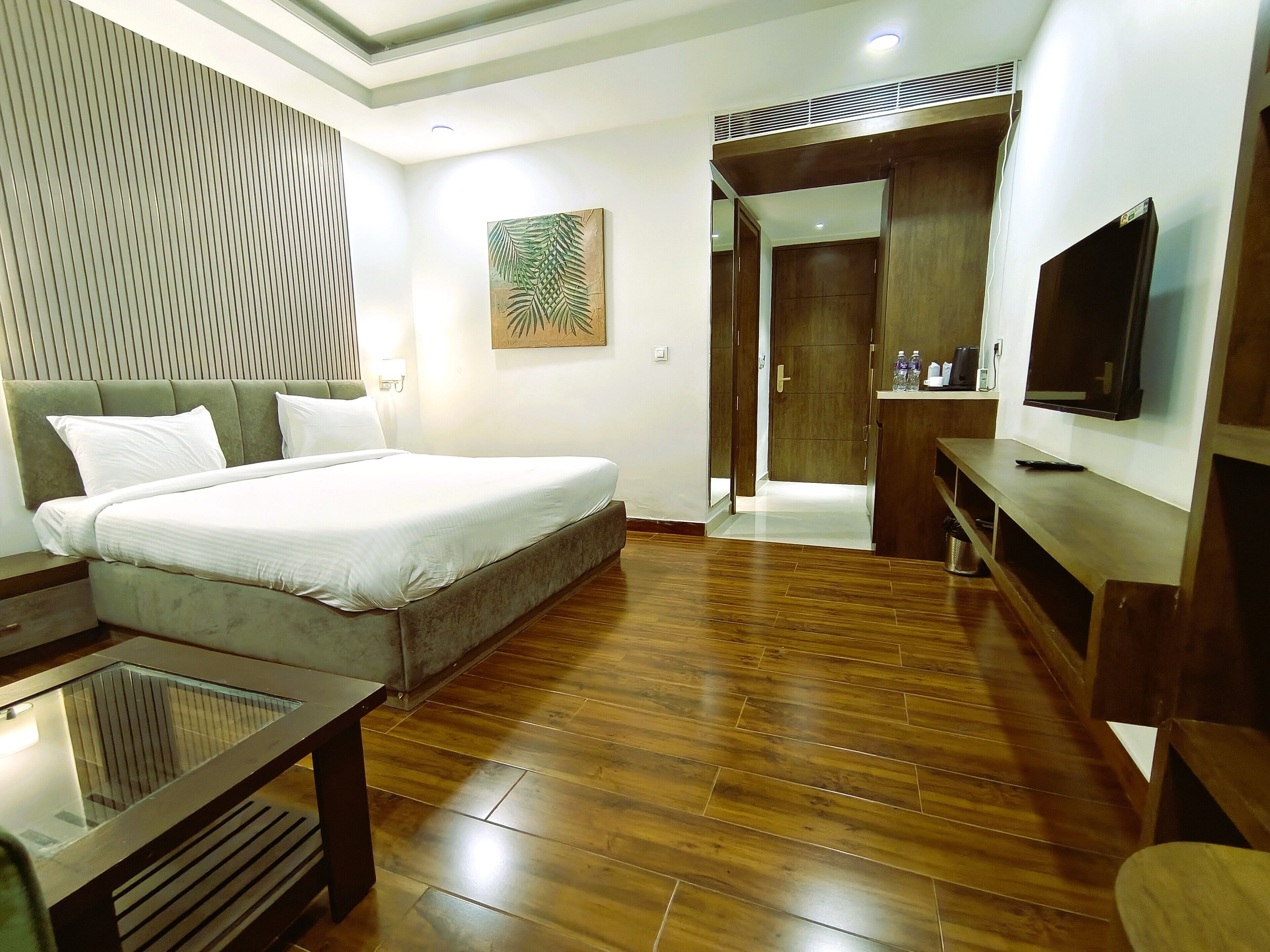 A modern bedroom with a large bed, a TV, a wooden floor, and a door leading to a bathroom.